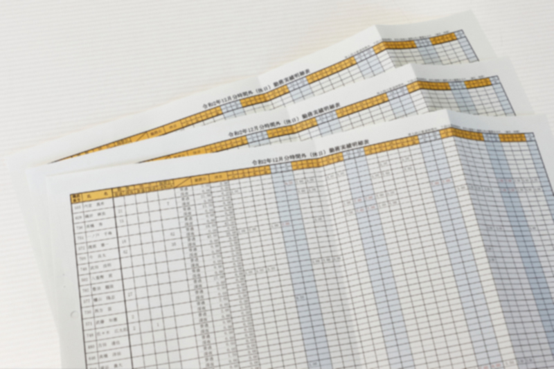 イメージ：時間外（休日）勤務実績明細表。従来は紙の申請書を手作業で表にまとめていた